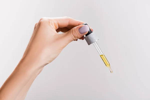 Cropped view of woman holding pipette with oil isolated on grey — Stock Photo