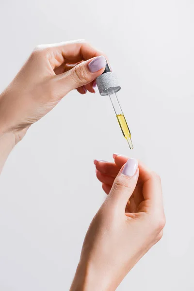 Cropped view of woman applying oil from pipette on fingernails isolated on grey — Stock Photo