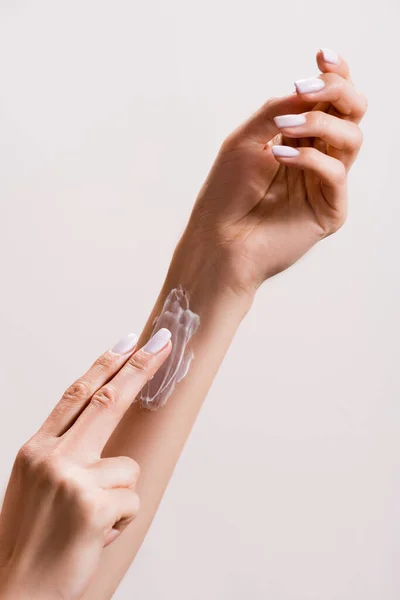 Vista recortada de la mujer aplicando crema de manos en el brazo aislado en gris - foto de stock