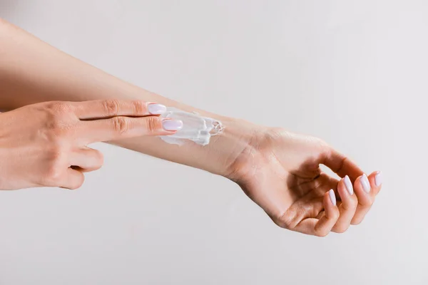 Cropped view of woman applying hand cream on arm isolated on grey — Stock Photo