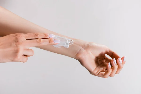 Vue recadrée de la femme appliquant de la crème pour les mains sur le bras isolé sur gris — Photo de stock