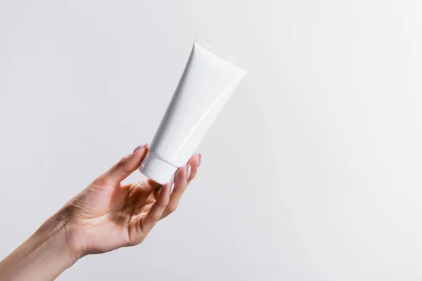Cropped view of woman holding tube of hand cream isolated on grey — Stock Photo