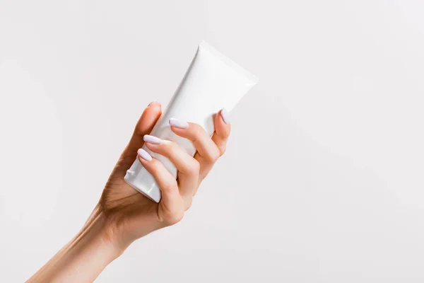 Cropped view of woman holding tube of hand cream isolated on grey — Stock Photo