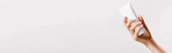 Vista ritagliata di donna tenuta tubo di crema per le mani isolato su grigio, banner — Foto stock