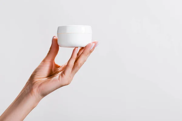 Cropped view of woman holding container of hand cream isolated on grey — Stock Photo