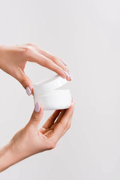 Cropped view of woman opening container of hand cream isolated on grey — Stock Photo