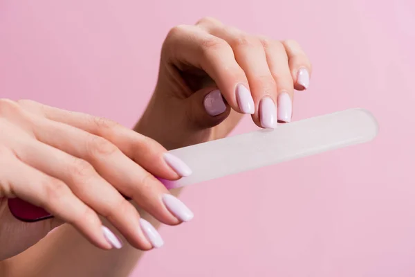 Vista recortada de la mujer usando lima de uñas aislado en rosa - foto de stock