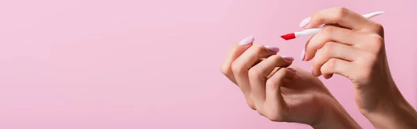 Vista cortada de mulher segurando cutícula empurrador isolado em rosa, banner — Fotografia de Stock
