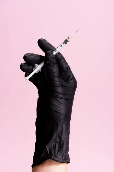 Vue recadrée de la main en gant de latex noir avec seringue isolée sur rose — Photo de stock