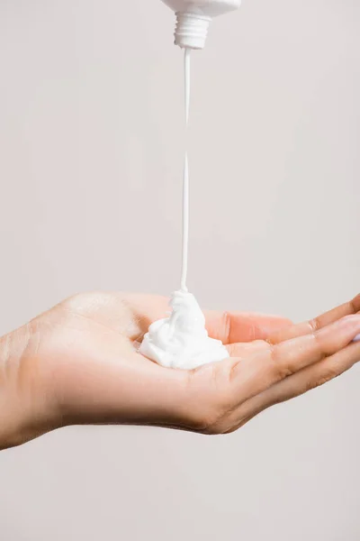 Cropped view of woman squeezing hand cream isolated on grey — Stock Photo