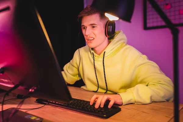 Confused gamer in headset using computer on blurred foreground — Stock Photo