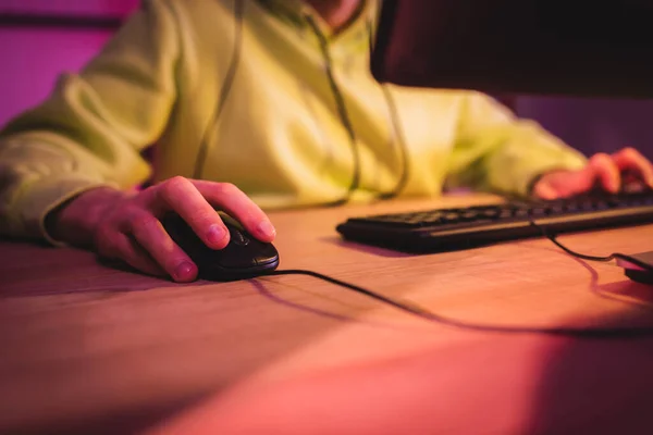 Vista ritagliata del giocatore utilizzando il mouse del computer vicino alla tastiera su sfondo sfocato — Foto stock