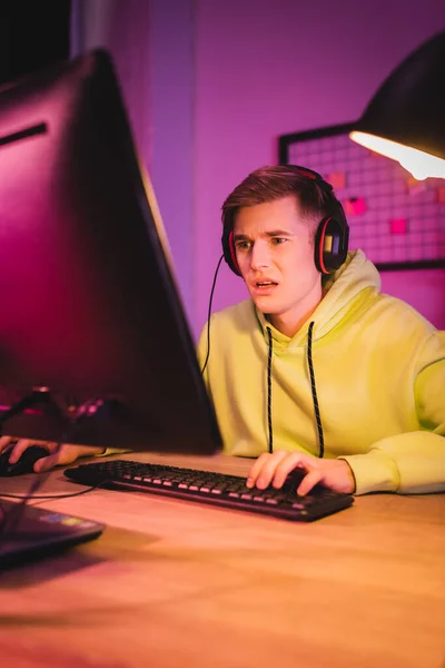 Verwirrter Mann im Headset benutzt Computer beim Spielen von Videospielen zu Hause — Stockfoto