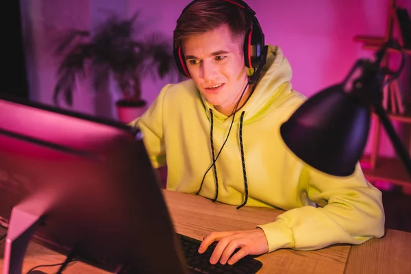 Giocatore sorridente in auricolare che gioca al videogioco sul computer in primo piano sfocato — Foto stock