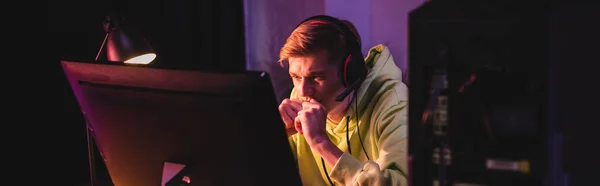 Stressed gamer in headset looking at computer monitor near system unit on blurred foreground, banner — Stock Photo