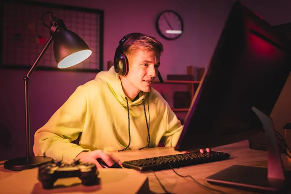 Giocatore sorridente in auricolare utilizzando il computer vicino joystick sulla scatola della pizza in primo piano sfocato — Foto stock