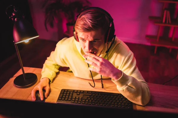 Jugador nervioso en auriculares usando computadora en primer plano borroso - foto de stock