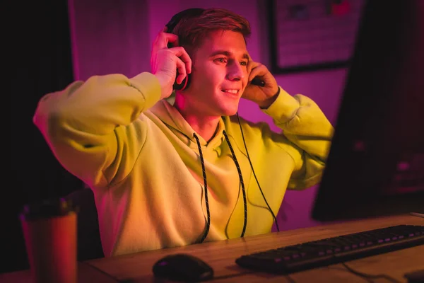 Jugador sonriente con auriculares cerca de la computadora y el café para ir en primer plano borrosa - foto de stock