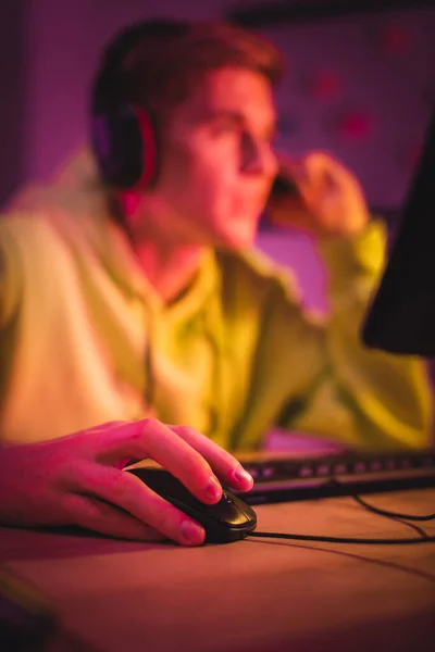 Computer mouse in hand of gamer in headset on blurred background — Stock Photo