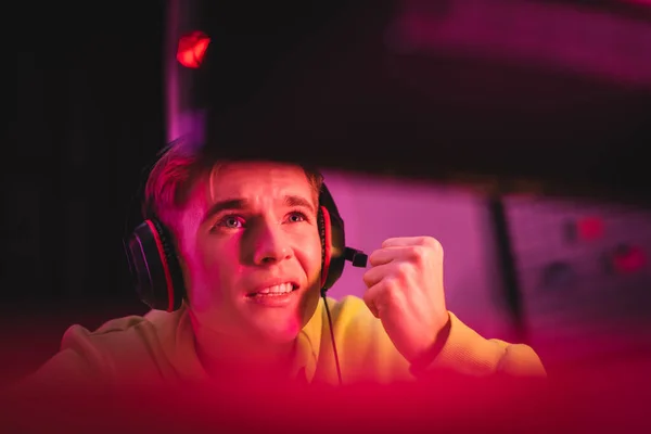 Jugador sonriente usando auriculares cerca del monitor de la computadora en primer plano borroso - foto de stock