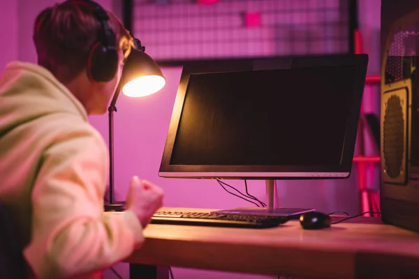 Computer monitor with blank screen near gamer in headset showing yeah gesture on blurred foreground — Stock Photo