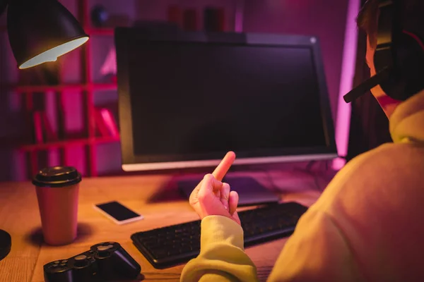 KIEW, UKRAINE - 21. AUGUST 2020: Gamer im Headset mit Mittelfinger am Steuerknüppel, Coffee to go und Computer auf verschwommenem Hintergrund — Stockfoto