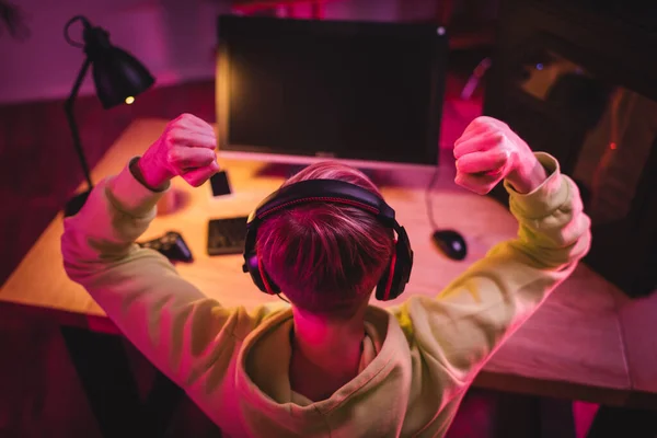 Vista aérea del jugador en auriculares que muestran sí gesto cerca de la computadora y joystick sobre fondo borroso - foto de stock