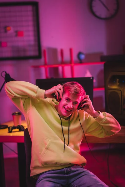 Cheerful gamer holding headphones near computer and joystick on blurred background — Stock Photo