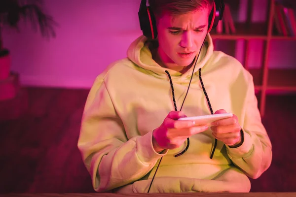 Worried gamer in headphones using smartphone at home — Stock Photo