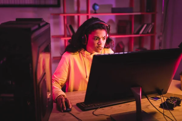 QUIIV, UCRÂNIA - 21 DE AGOSTO DE 2020: Gamer afro-americano confuso no fone de ouvido usando o computador perto do joystick e da caixa de pizza na mesa — Fotografia de Stock