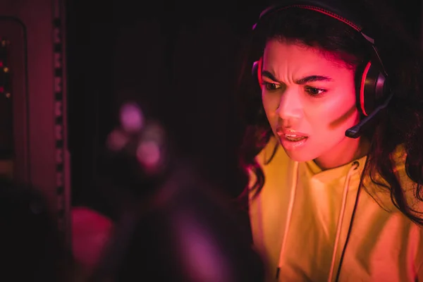 Mujer afroamericana pensativa en auriculares mirando hacia otro lado cerca de la unidad del sistema de la computadora sobre fondo borroso - foto de stock