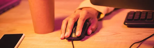 Vista recortada del jugador utilizando el ratón de la computadora cerca de teléfono inteligente y café para ir a la mesa, bandera - foto de stock