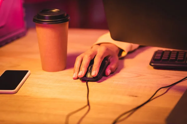 Vista recortada del jugador usando el ratón de la computadora cerca del teléfono inteligente con pantalla en blanco y café para llevar - foto de stock