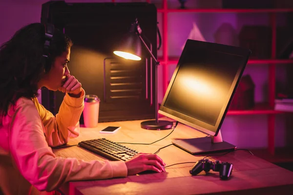 African american gamer using computer near gamepad, coffee to go and smartphone on blurred background — Stock Photo