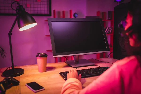 Computador com tela em branco, joystick e café para ir perto do jogador americano africano em primeiro plano desfocado — Fotografia de Stock