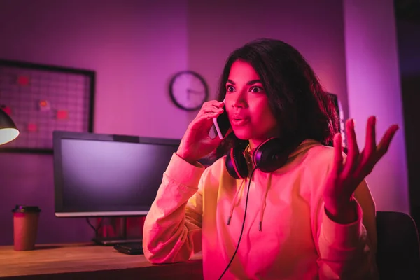 African american gamer talking on smartphone near computer on blurred background — Stock Photo