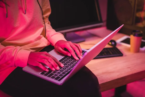 Cropped view of woman using laptop near computer and coffee to go on blurred background — Stock Photo