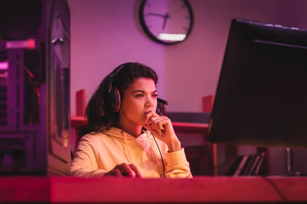 Femme afro-américaine pensive dans un casque regardant l'ordinateur sur le premier plan flou — Photo de stock