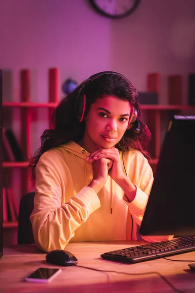 African american gamer in headset looking at camera near devices on blurred foreground — Stock Photo