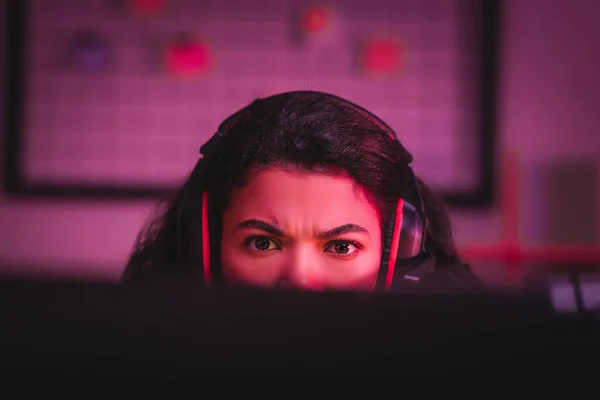 Fokussierter afrikanisch-amerikanischer Gamer im Headset, der auf verschwommenem Vordergrund auf den Computer blickt — Stockfoto