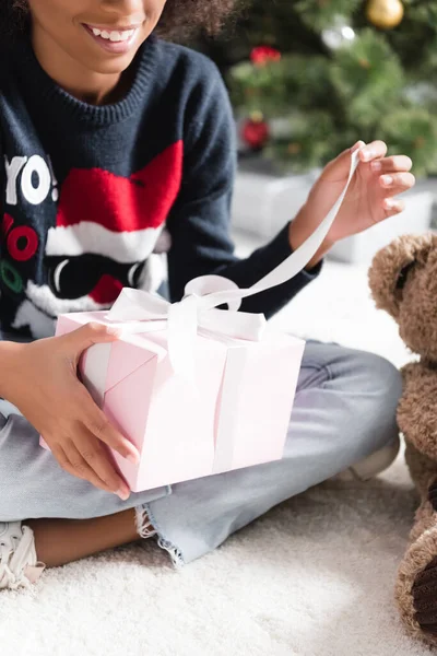 Partial view of smiling african american girl opening gift box on blurred background — Stock Photo