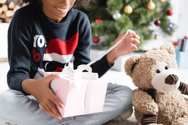 Cropped view of happy african american girl opening christmas present on blurred background — Stock Photo