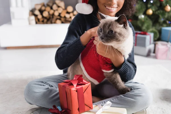 Vista cortada de afro americano menina abraçando gato enquanto sentado perto de caixas de presente no fundo borrado — Fotografia de Stock