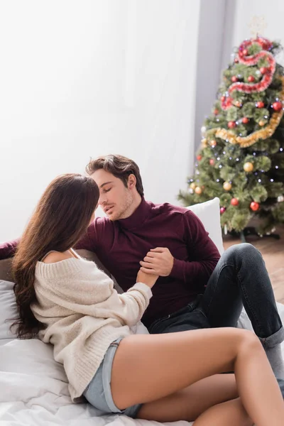 Paar in Pullovern hält Händchen neben geschmücktem Weihnachtsbaum auf verschwommenem Hintergrund — Stockfoto
