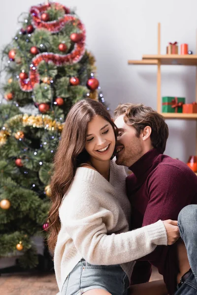 Joyful couple in sweaters embracing near christmas tree on blurred background — Stock Photo