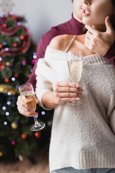 Vista ritagliata di coppia che tiene i bicchieri con champagne vicino all'albero di Natale su sfondo sfocato — Foto stock