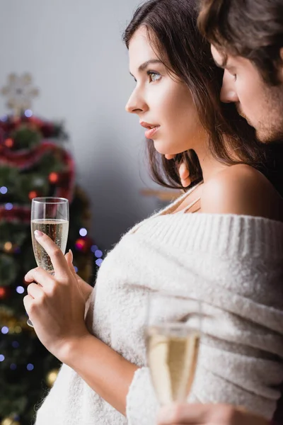 Coppia che tiene i bicchieri con champagne vicino albero di Natale su sfondo sfocato — Foto stock