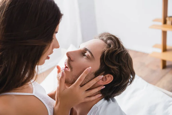 Сексуальная женщина трогает лицо страстного мужчины в спальне — стоковое фото