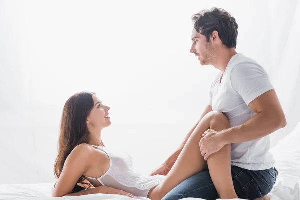 Side view of passionate man looking at pleased girlfriend in bodysuit — Stock Photo