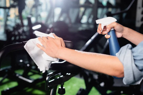 Teilansicht einer Verkäuferin beim Putzen von Sportgeräten im Fitnessstudio im unscharfen Vordergrund — Stockfoto